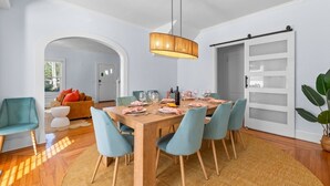 A dining area with a wooden table set for six, surrounded by six chairs. There is a large plant to the right and a sliding door with frosted glass panels to the right of the table. - Heated Pool~Hottub~Arcade~120"Screen~BBQ~Firepit (Bradenton)