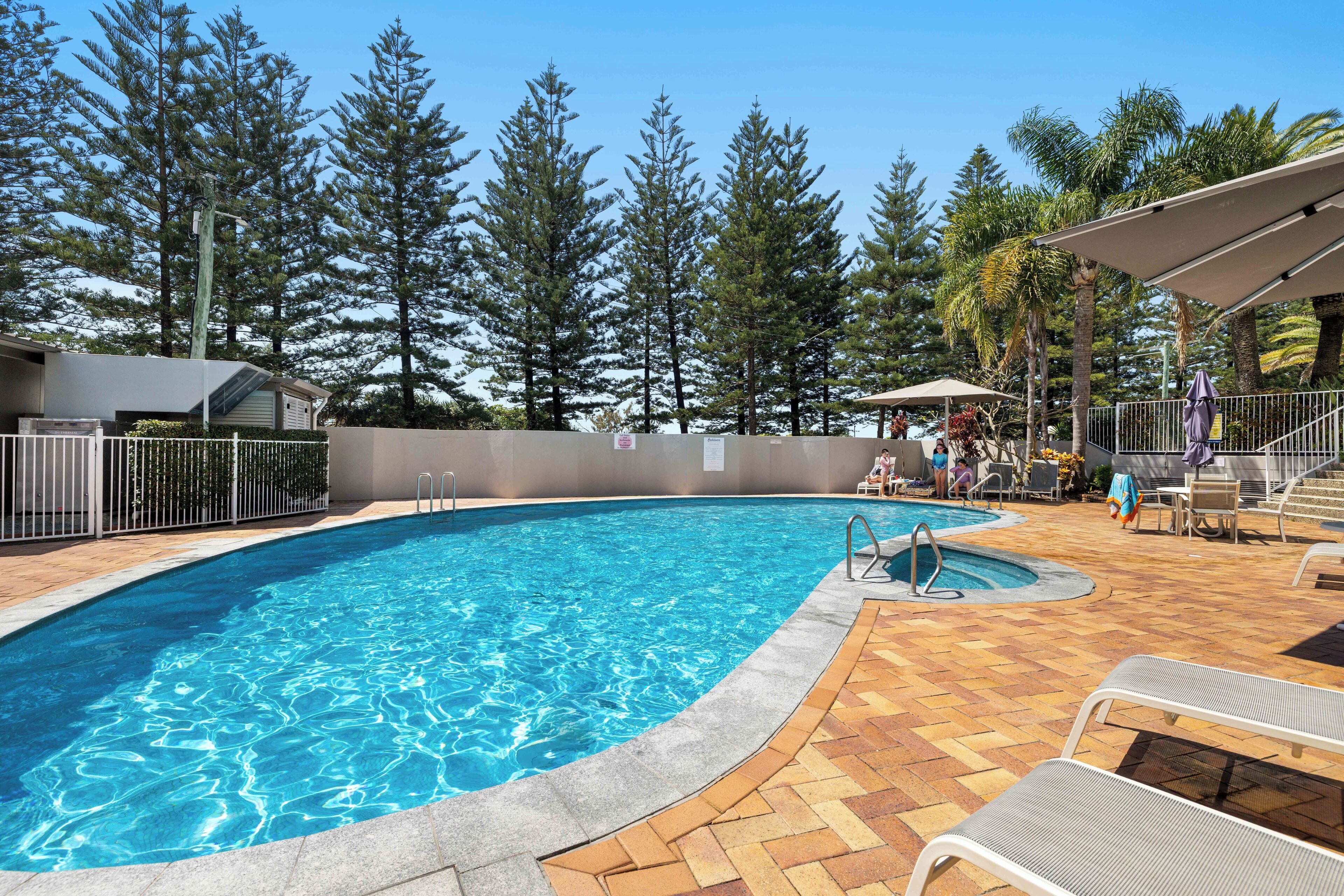 Une piscine dotée d’une terrasse carrelée, entourée d’une cl ôture et d’arbres.