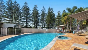 A swimming pool with a tiled deck, surrounded by a fence and trees.