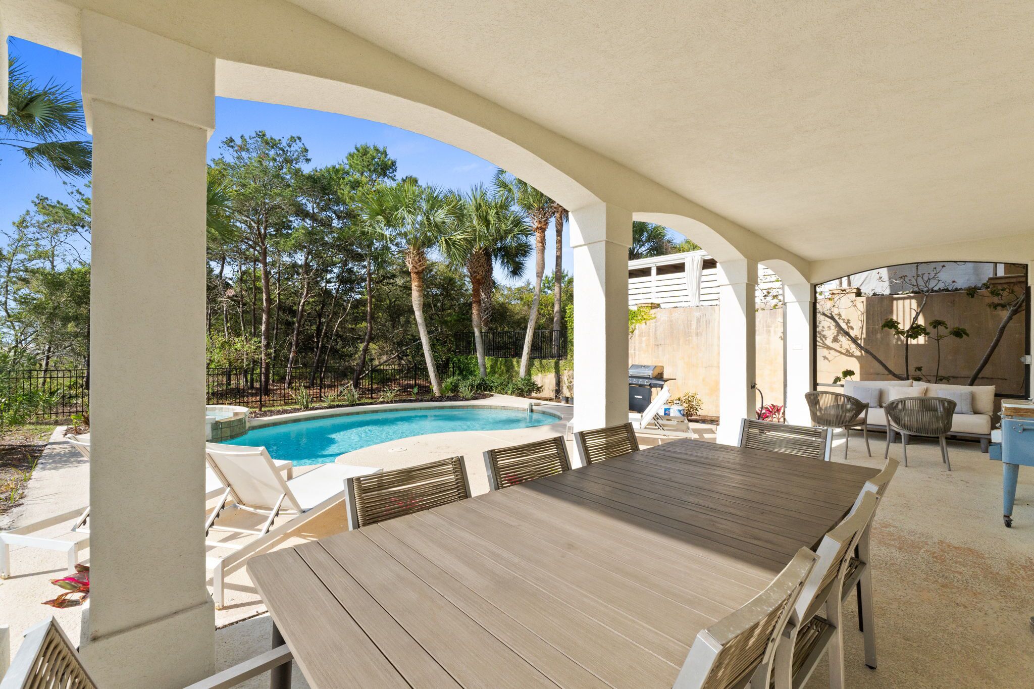 A covered outdoor area with a pool, lounge chairs, and a dining table.