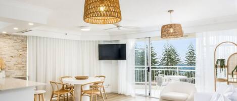Ein modernes Wohnzimmer mit Essbereich, großen Fenstern und einem Balkon mit Blick auf Bäume.