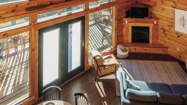 Interior de una cabaña con una gran mesa de comedor, un sofá, una chimenea y un ventilador de techo.