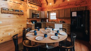Cocina de estilo cabaña de madera con una mesa redonda para seis personas, rodeada de sillas negras.