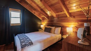 Un dormitorio acogedor tipo cabaña de madera, con cama, lámparas de noche y mesita de noche.