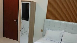 A hotel room with a bed, a wardrobe, and a wooden panel wall. - Kedaton Home Kostel (Surakarta)