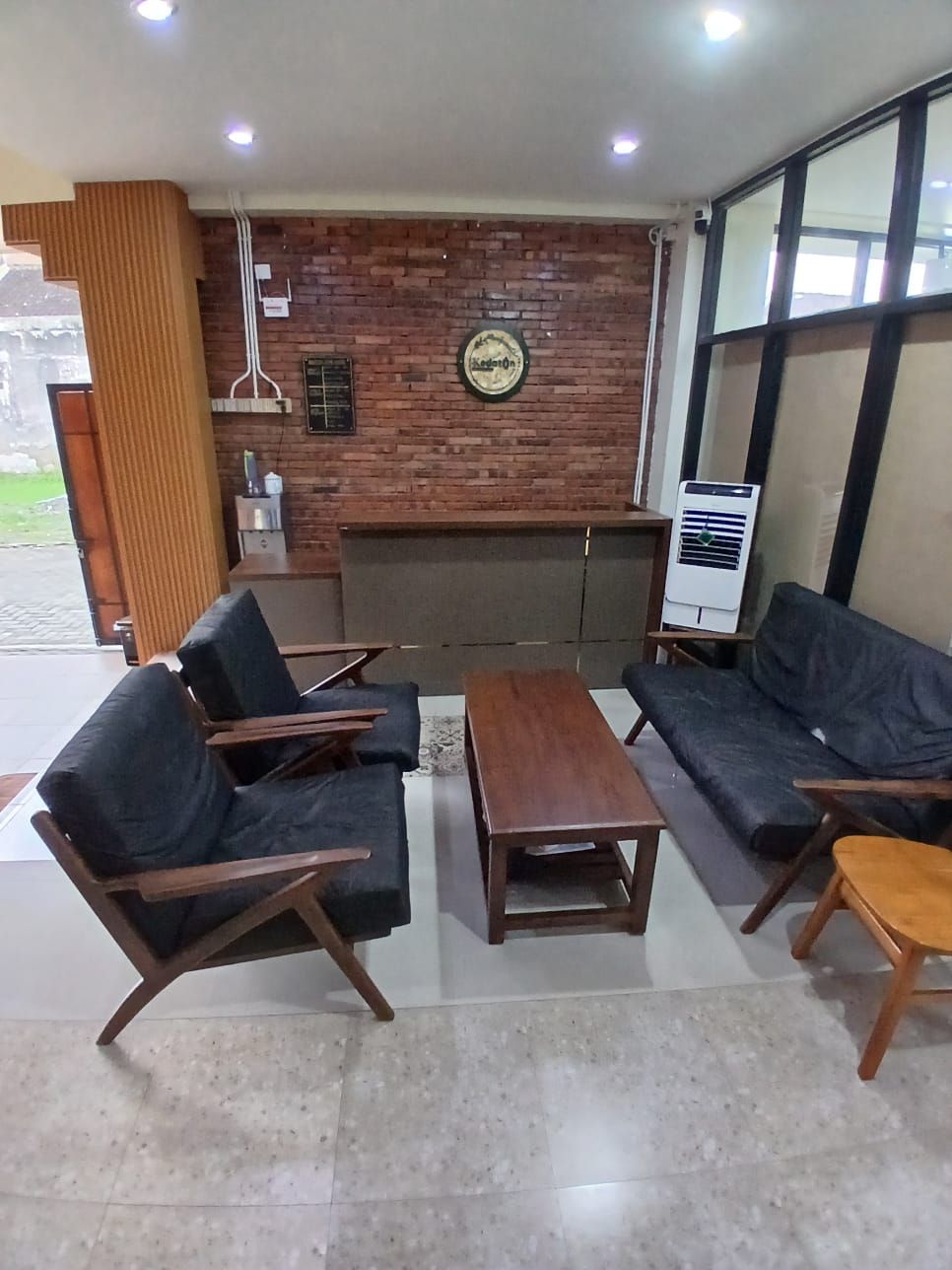 Eine moderne Lobby mit Backsteinwand, einer runden Uhr und einer Sitzecke mit Sofas und einem Couchtisch.