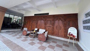 A lobby with a checkered floor, a wooden wall with intricate carvings, a seating area with sofas and a table, and a signboard. - Kedaton Home Kostel (Surakarta)
