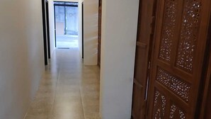 A hallway with a tiled floor, a wooden door with intricate carvings, and a recessed ceiling light. - Kedaton Home Kostel (Surakarta)
