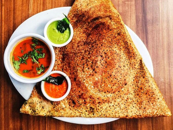 A plate with a folded dosa, two chutneys, and a small bowl of sauce.