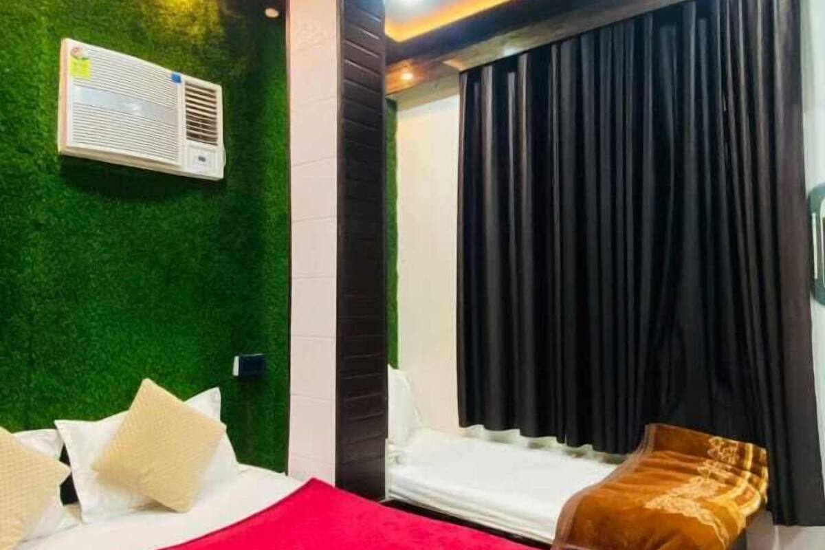 Une chambre d’hôtel avec deux lits, un mur vert, un ventilateur de plafond, un appareil de climatisation et une fenêtre avec des rideaux noirs.