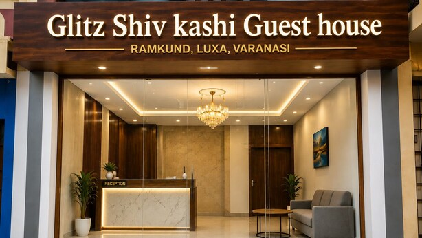 A hotel reception area with a reception desk, a chandelier, a sofa, and a potted plant. - Shiv Kashi P Guest House By Glitz Hotels (Varanasi)