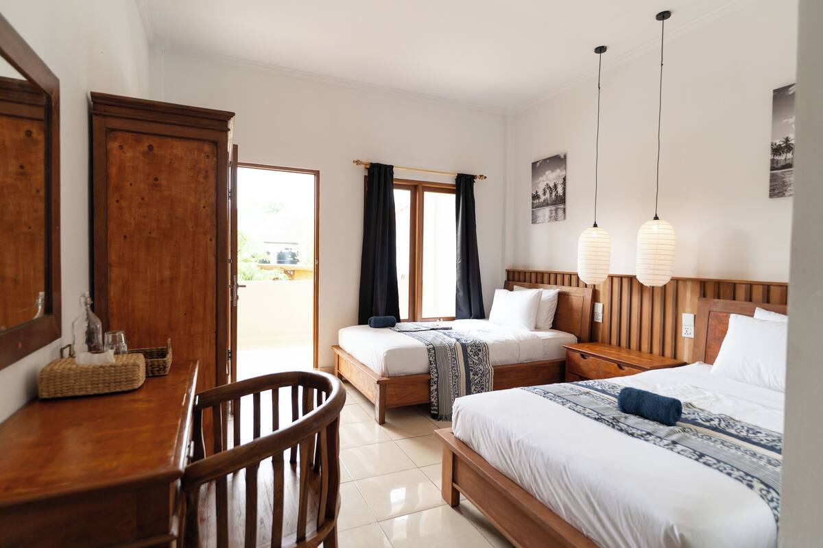 A hotel room with two beds, a wooden desk, and a chair.