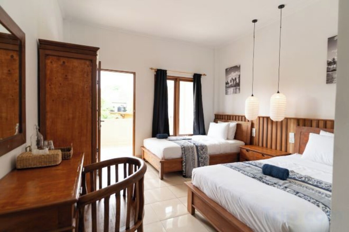 A bedroom with a wooden desk, two beds, a chair, and a view through a door.