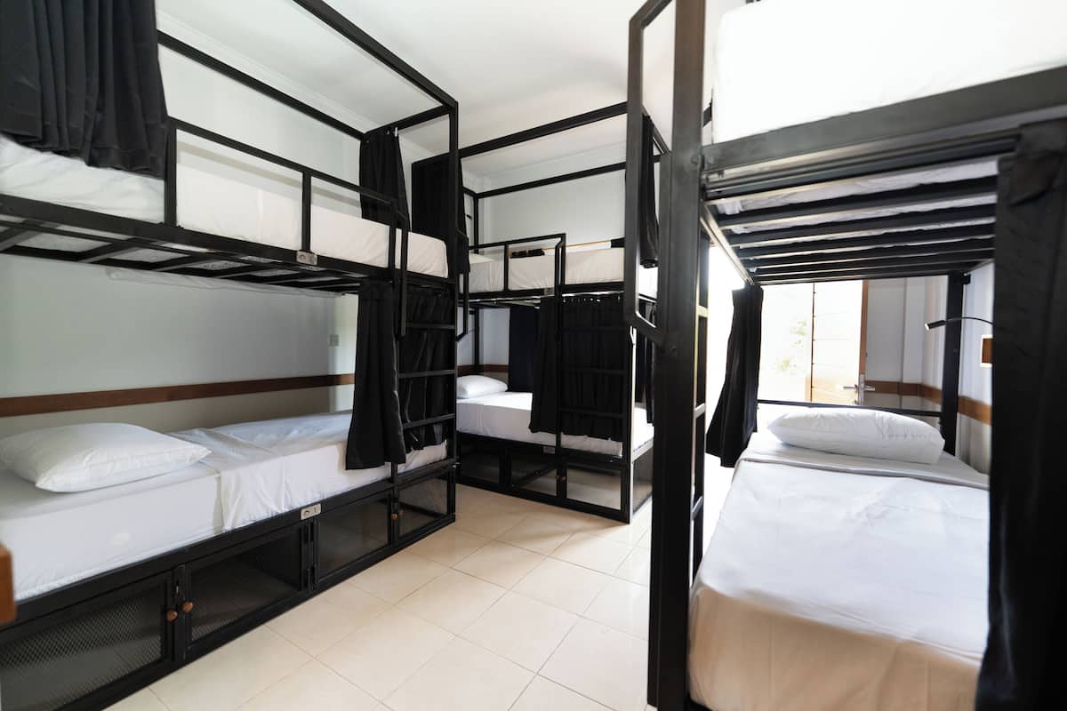 A dormitory-style room with bunk beds, a wooden headboard, and a window with curtains.