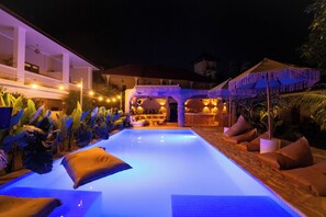 A nighttime pool area with a clear view of the pool, lounge chairs, and a bar area. - Mad Monkey Uluwatu (Pecatu)