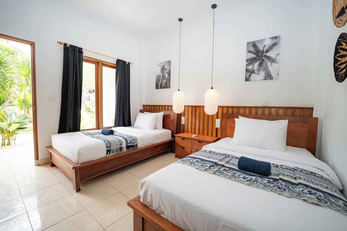 A hotel room with two beds, a wooden headboard, a nightstand, and a window with curtains.