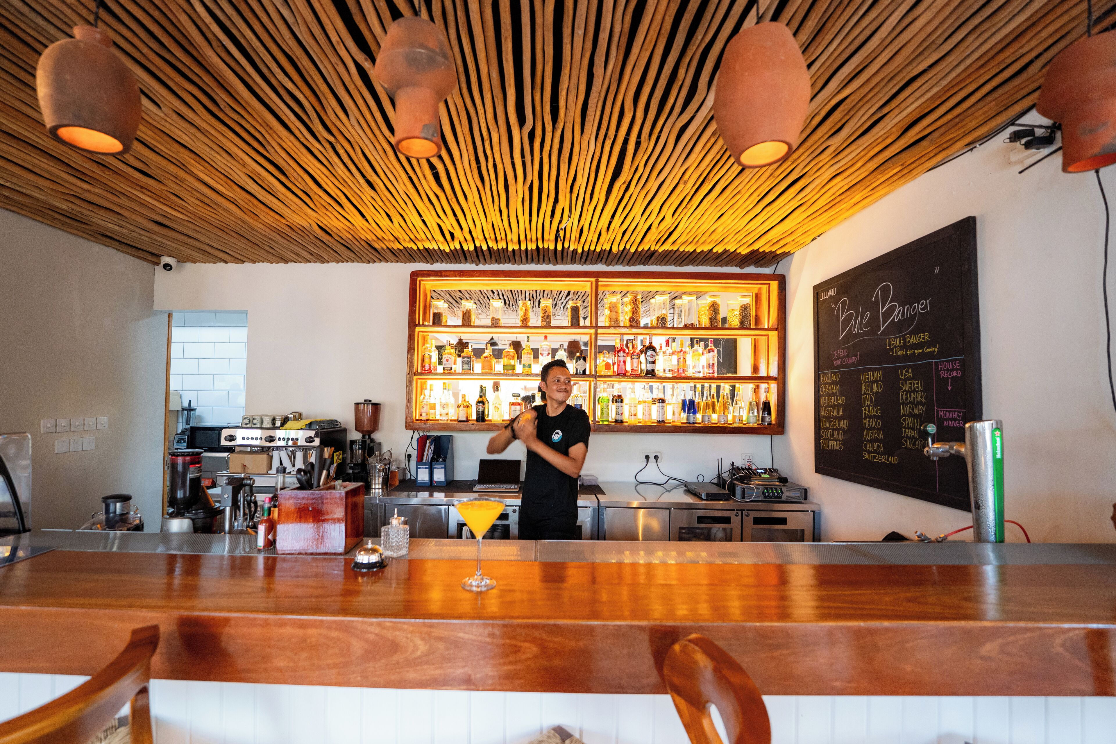Un bar con techo de madera, un cantinero y una pizarra que enumera diferentes bebidas.