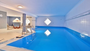 Ein Hallenbad mit blauem Boden, einer Leiter und einem Liegebereich.