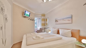 Ein Hotelzimmer mit Bett, Fernseher, einem Gemälde und einem Fenster mit Vorhängen.