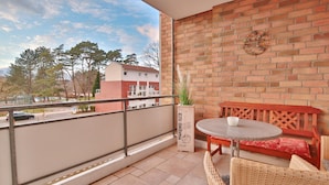 Ein Balkon mit rundem Tisch und Korbstühlen, eine Backsteinmauer und Blick auf Gebäude und Bäume.