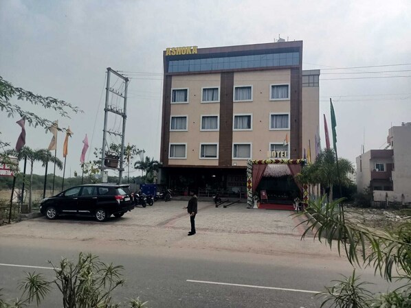 A multi-story hotel with a sign reading "ASHOKA HOTEL" and a flag display in front.