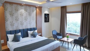 Una habitación de hotel con una cama grande, un escritorio, dos sillas, una ventana con cortinas y una pared con diseño floral.