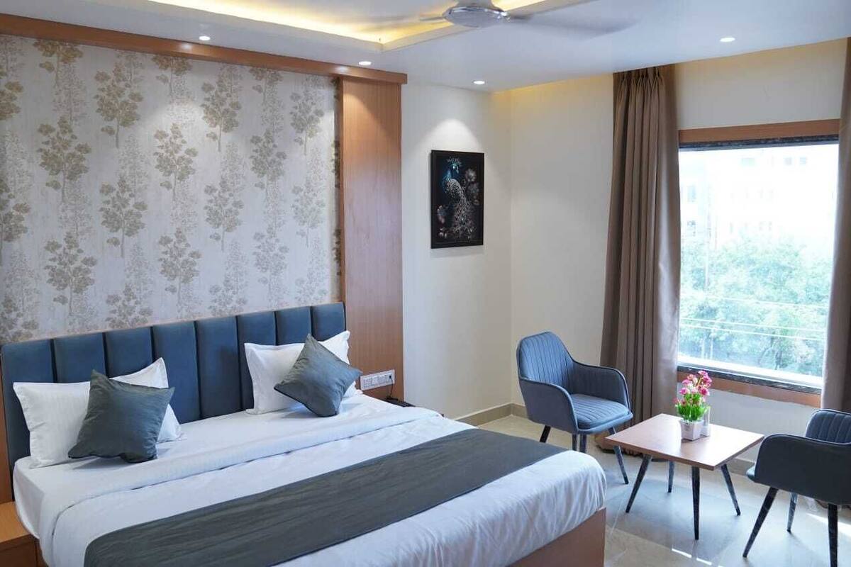 Hotelkamer met een groot bed, een bureau, twee stoelen, een raam met gordijnen en een bloemenmotief op de muur.