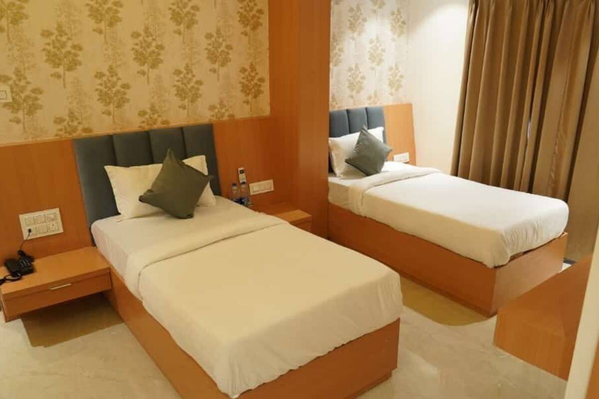 Een hotelkamer met twee bedden, elk met hoofdbord en kussens. Aan elke kant van de bedden staat een nachtkastje met een telefoon en een lamp.