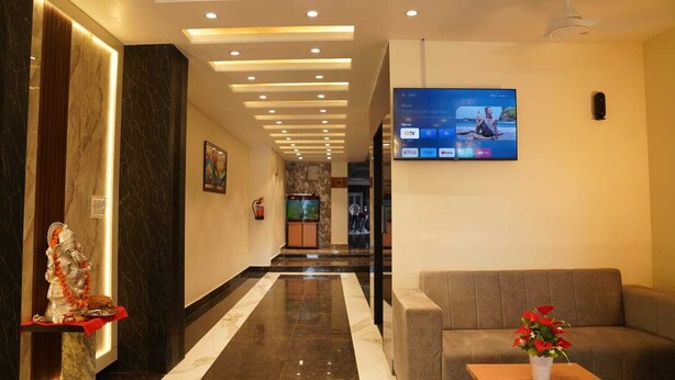 Vestíbulo de hotel con área de recepción, un sofá, una pantalla de televisión y una estatua decorativa.