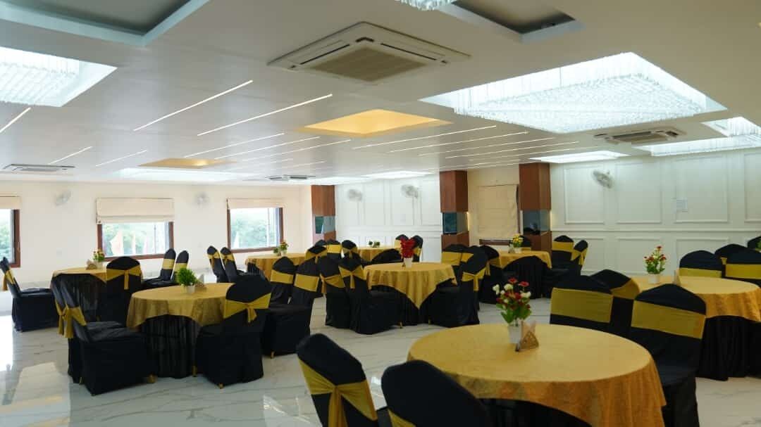 A banquet hall with round tables and black chairs, each with a gold sashed tablecloth.