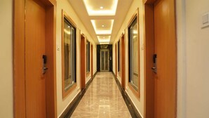 Un pasillo de hotel con puertas de madera, ventanas amplias y piso de baldosas.