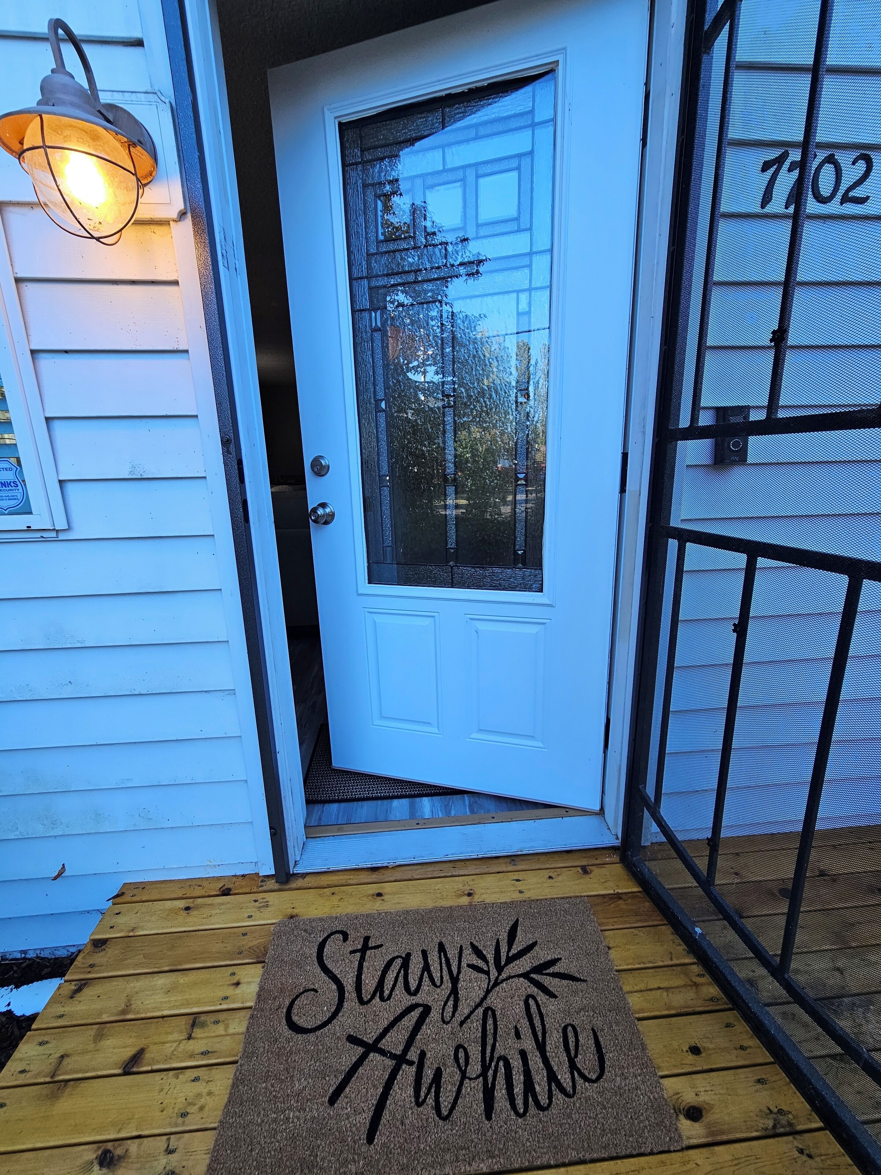 A white door with a glass panel, a metal gate, and a doormat with "Stay awhile" text.