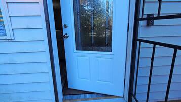 A white door with a glass panel, a metal gate, and a doormat with "Stay awhile" text.