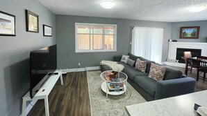 A living room with a TV, sofa, coffee table, fireplace, and a window with blinds.