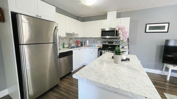 A modern kitchen with white cabinets, stainless steel appliances, a marble countertop, and a potted orchid.