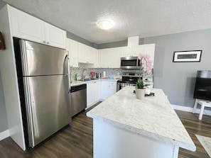 A modern kitchen with white cabinets, stainless steel appliances, a marble countertop, and a potted orchid. - Entire Guest Suite in Thetis Height (Victoria)