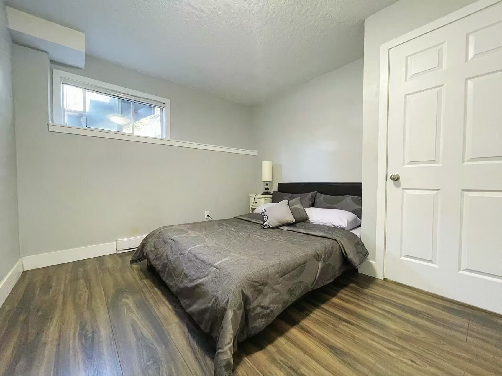 A bedroom with a bed, a nightstand, a lamp, and a window.