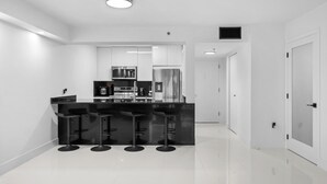 A modern kitchen with a black countertop, stainless steel appliances, and three black bar stools. - Luxury apartment in downtown Brickell with SEA view, Miami  (Miami)