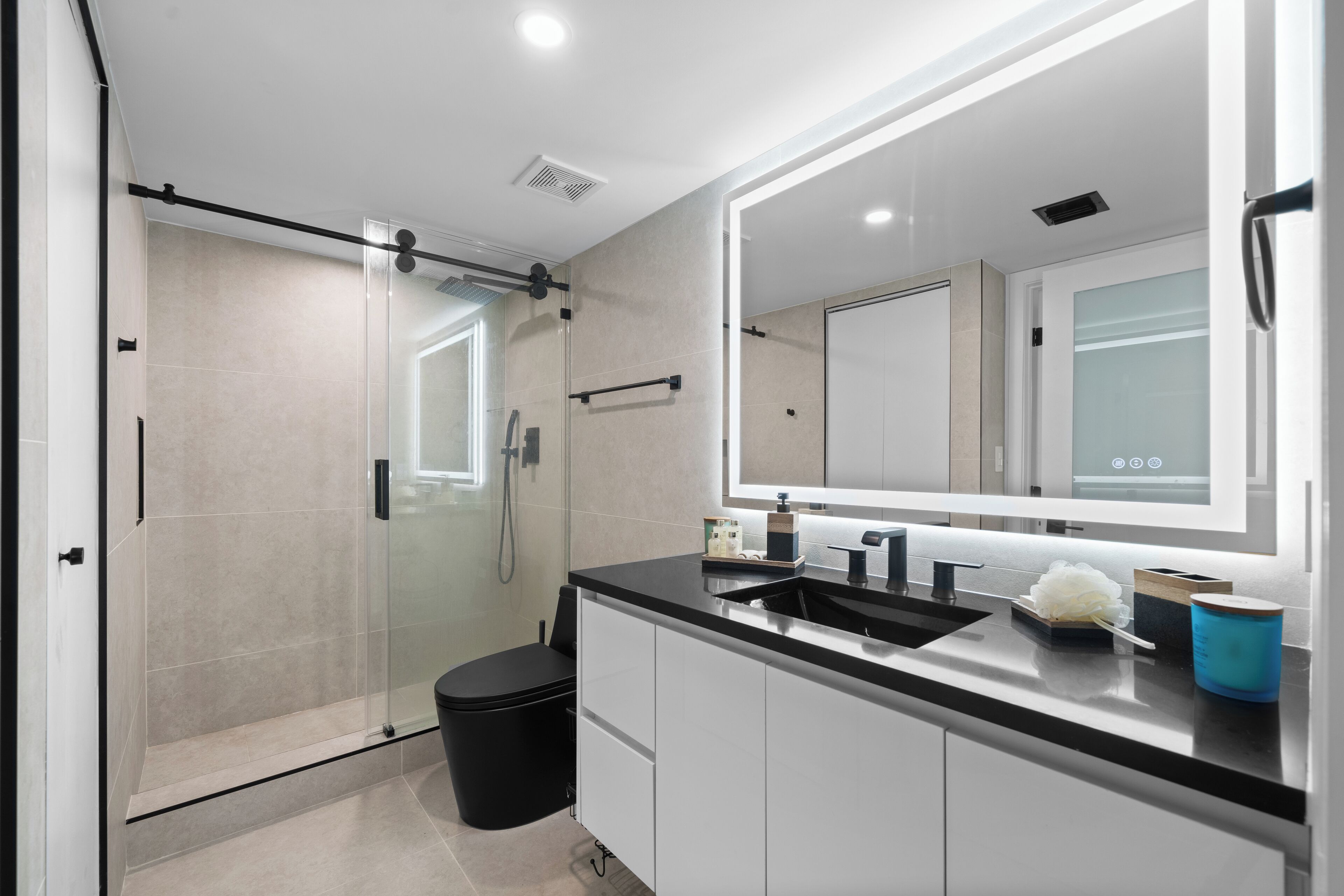 A modern bathroom with a glass shower enclosure, a black toilet, a white sink with a black countertop, and a large mirror above the sink.