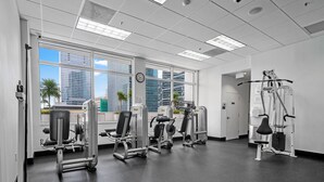 A gym with various exercise machines, large windows, and a view of city buildings. - Luxury apartment in downtown Brickell with SEA view, Miami  (Miami)