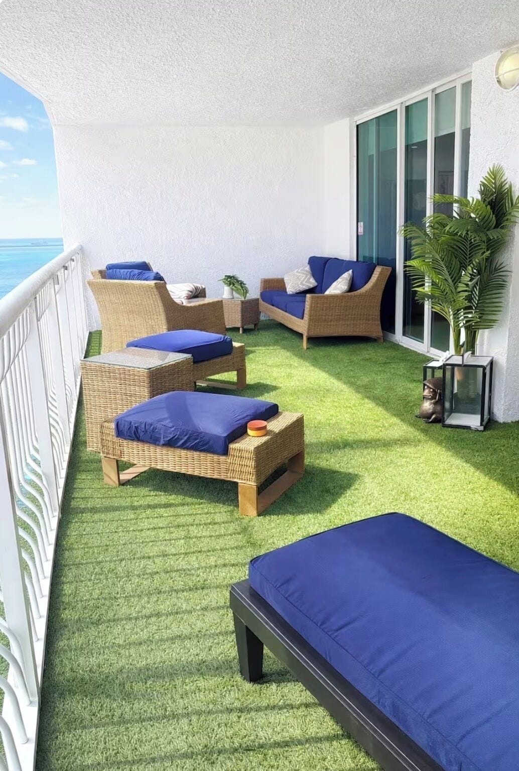 A balcony with wicker furniture, artificial grass, and a view of the sea.