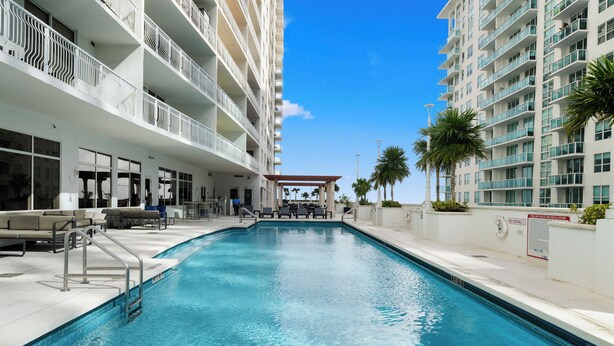 A swimming pool with a view of a multi-story building, outdoor seating, and palm trees. - Luxury apartment in downtown Brickell with SEA view, Miami  (Miami)