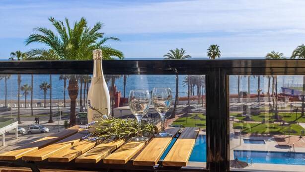 A table with a bottle and glasses, overlooking a pool and palm trees. - Aloha Playa 402 - Terraze, Swimming Pool, Sea Views. Benalmadena (Benalmádena)