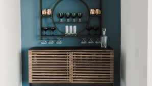 A dark teal wall with a wooden console table displaying glassware and decorative items. - Modern Townhome with Skyline Views, Heated Balcony & Curated Art in Downtown DSM (Des Moines)