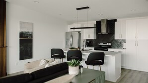 A modern kitchen with white cabinets, a central island, and black chairs. - Modern Townhome with Skyline Views, Heated Balcony & Curated Art in Downtown DSM (Des Moines)