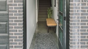 A narrow hallway with a wooden bench, a glass door, and a brick wall. - Modern Townhome with Skyline Views, Heated Balcony & Curated Art in Downtown DSM (Des Moines)