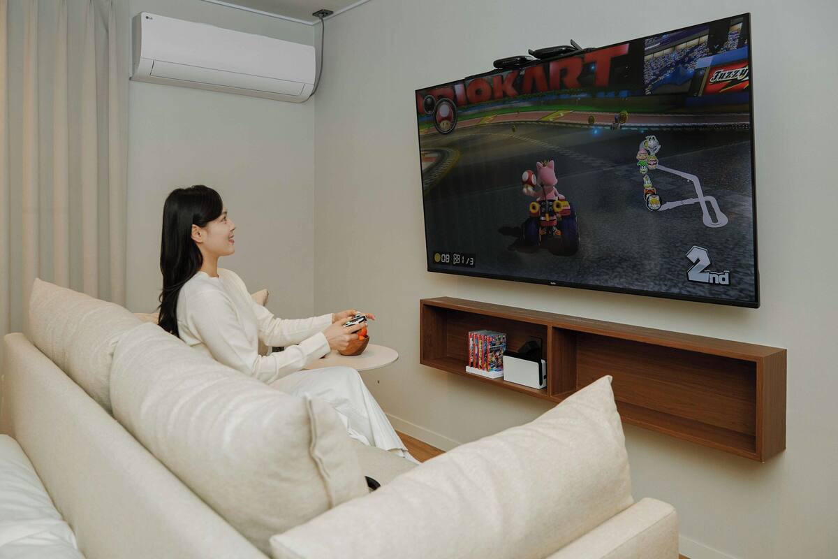 Una persona jugando un videojuego de carreras en un televisor grande montado en la pared.