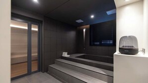 A modern bathroom with a large bathtub, a glass shower enclosure, and a set of stairs leading to a shower area. - Anook Hotel Yeongdengpo (Seoul)