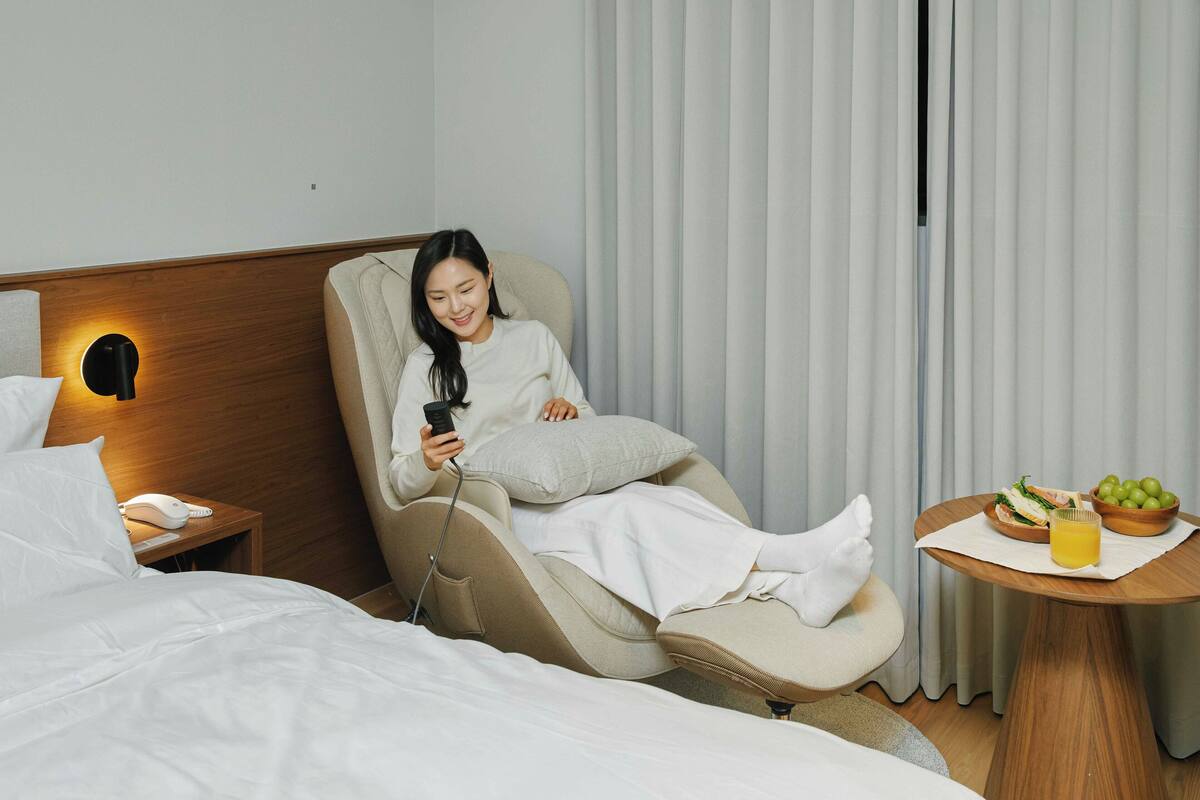 Habitación de hotel con sillón de masaje, mesita de noche con teléfono y una pequeña mesa con frutero y jugo.