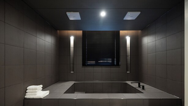 A modern bathroom with a rectangular bathtub, two wall-mounted lights, and a stack of white towels on the floor. - Anook Hotel Yeongdengpo (Seoul)